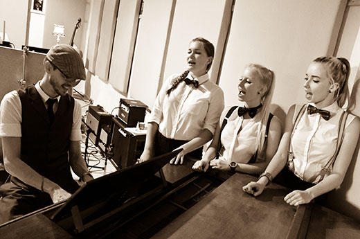 Drei Mädchen singend stehend am Klavier und ein Pianist
