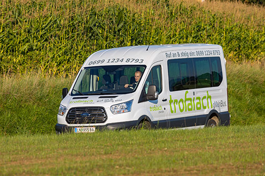 Der Gmeinbus fährt auf einer Gemeindestraße - im Hintergrund ein Maisfeld